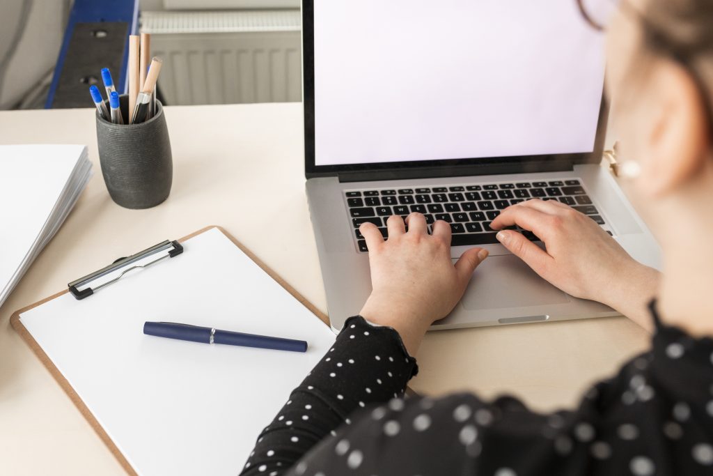 Mujer escribiendo en un ordenador portátil con un blog de notas al lado. Concepto de comunicación médica y científica.