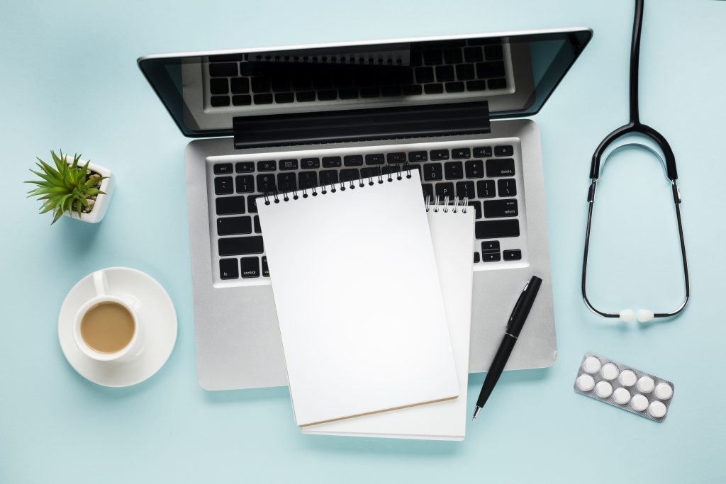 Pórtatil con bloc de notas en entorno médico. Concepto de comunicación médica y redacción científica.